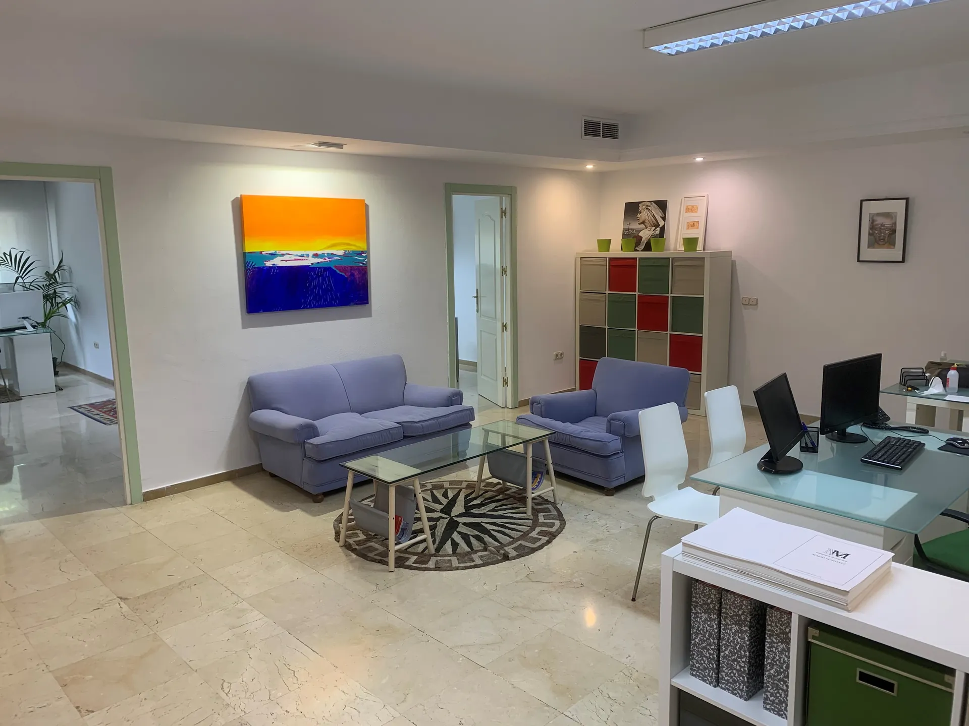 Reception area with two blue sofas, a glass coffee table and desks with computer screens, in the office photograph published on MMR Consultant's website