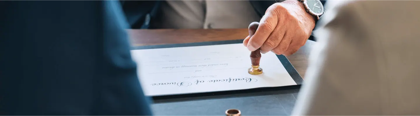 En hånd trykker et stempel på et signert dokument på et skrivebord