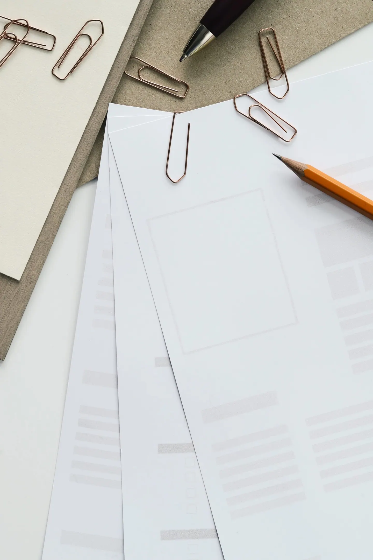 Sheets of paper fanned out on a desk with paper clips, a pen and a pencil